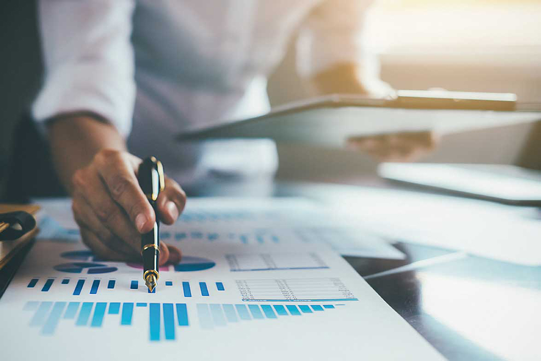 A person creating a set of graphs on a table while holding a clipboard with paper documents in it.
