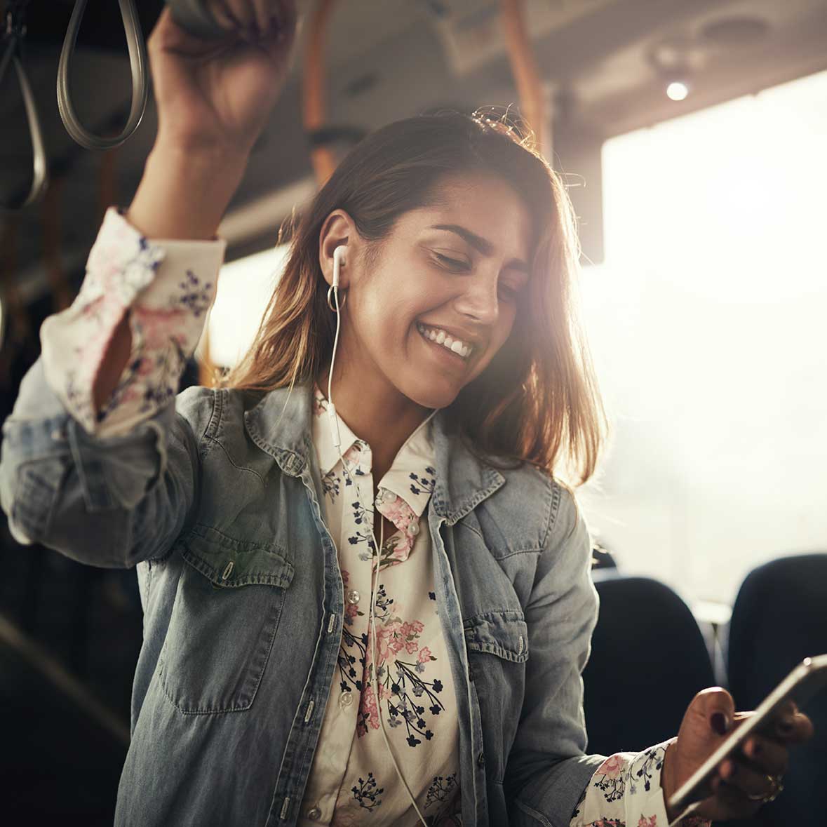 A lady holding a phone in one hand while grabbing a top handle with her other hand on a bus or train.