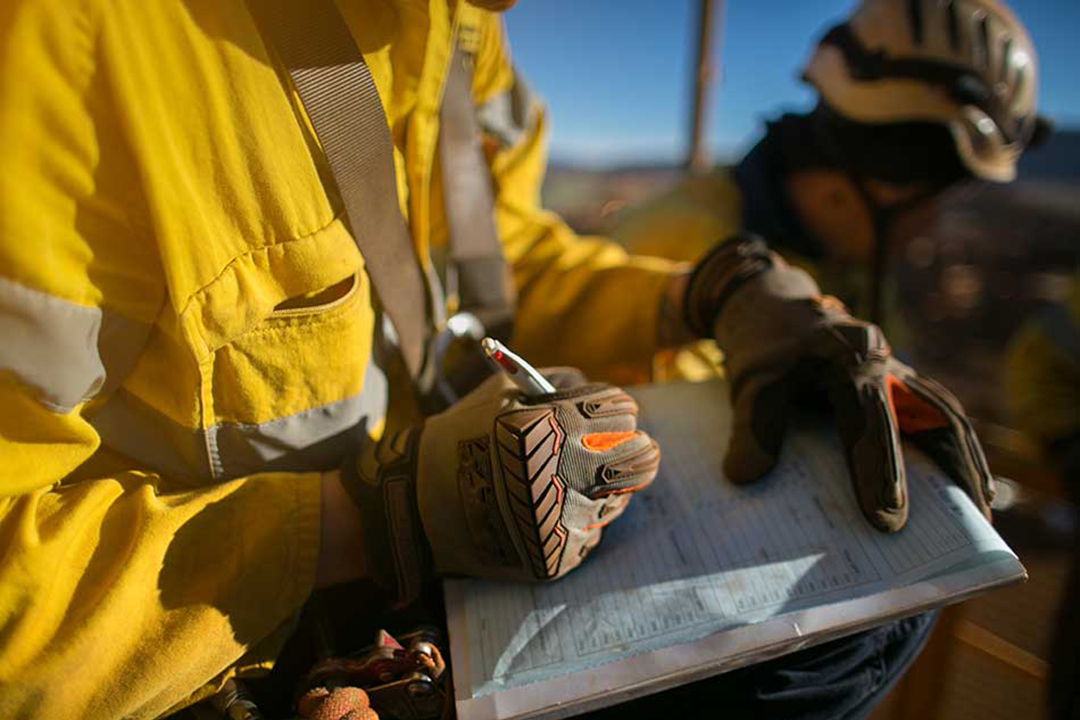 A person wearing reflective jacket and gloves writing on a clipboard.