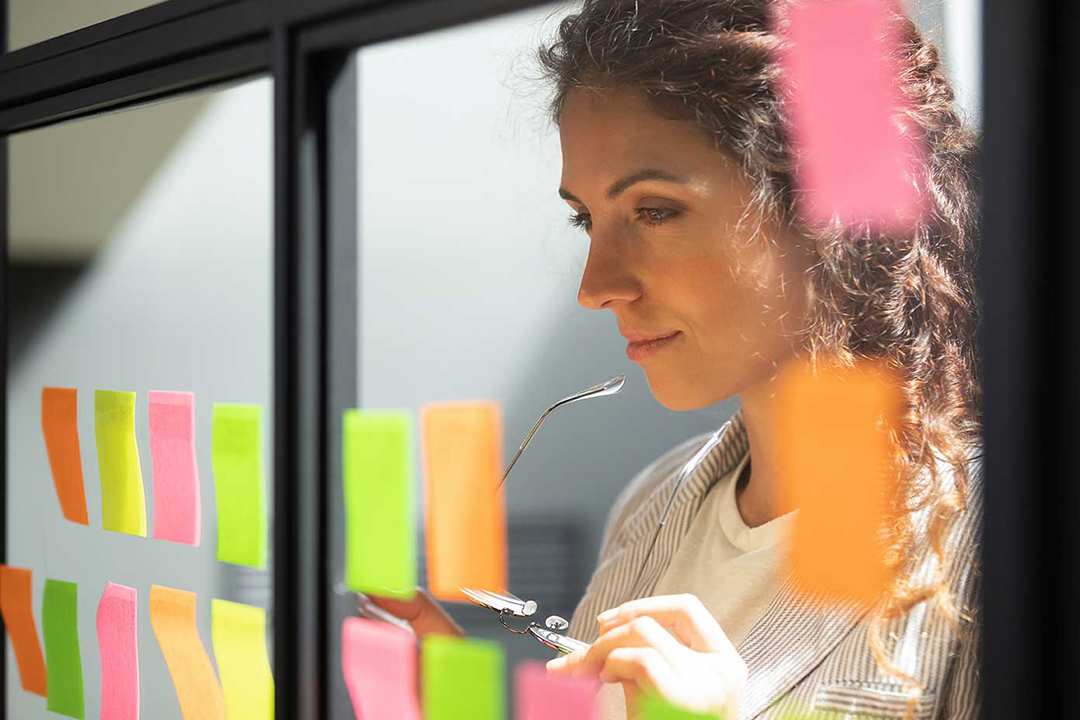 A lady looking at sticky notes places on a glass board.